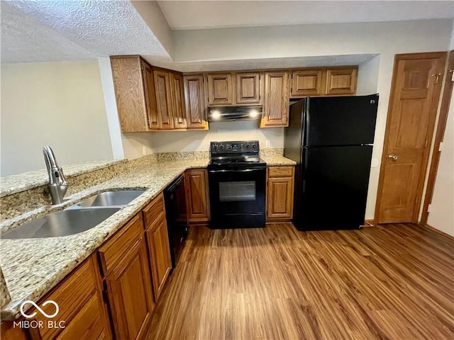 35 Northridge Ct, Brownsburg, IN 46112 - kitchen with black appliances, under cabinet range hood, wood finished floors, brown cabinetry, and light stone countertops