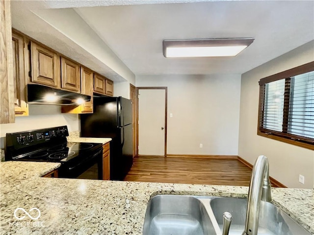 35 Northridge Ct, Brownsburg, IN 46112 - kitchen with black appliances, under cabinet range hood, wood finished floors, brown cabinetry, and light stone countertops
