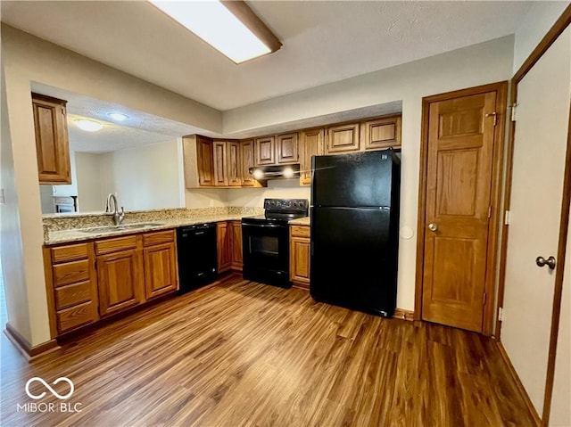 35 Northridge Ct, Brownsburg, IN 46112 - kitchen with black appliances, under cabinet range hood, wood finished floors, brown cabinetry, and light stone counters