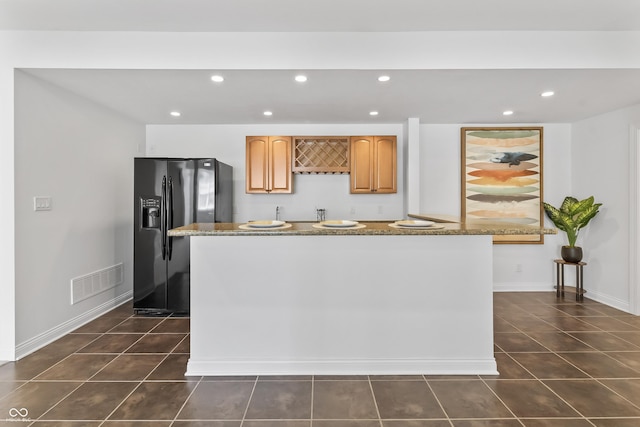 9877 Wading Crane Ave, Fishers, IN 46055 - kitchen with black fridge with ice dispenser, dark tile patterned floors, recessed lighting, dark stone countertops, and a center island