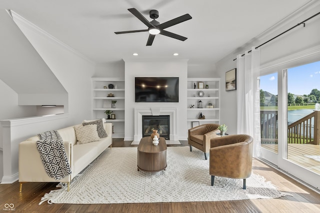 9877 Wading Crane Ave, Fishers, IN 46055 - living area with wood finished floors, a fireplace with flush hearth, a ceiling fan, crown molding, and built in shelves