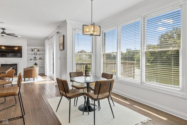 9877 Wading Crane Ave, Fishers, IN 46055 - dining room featuring crown molding, a glass covered fireplace, built in features, wood-type flooring, and a ceiling fan