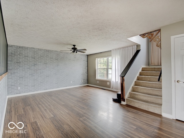 3902 Jekyll Ct, Indianapolis, IN 46237 - unfurnished living room with brick wall, ceiling fan, stairway, wood finished floors, and a textured ceiling