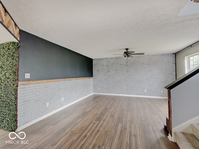 3902 Jekyll Ct, Indianapolis, IN 46237 - empty room featuring brick wall, a ceiling fan, a textured ceiling, wood finished floors, and stairs