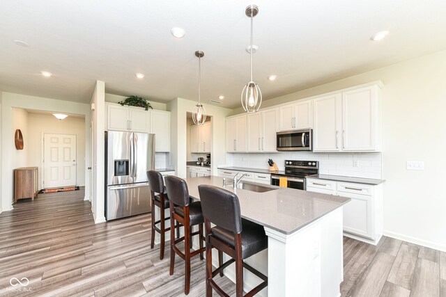 7101 Oak Trace Ln, Brownsburg, IN 46112 - kitchen featuring appliances with stainless steel finishes, a center island with sink, tasteful backsplash, a kitchen bar, and light wood finished floors