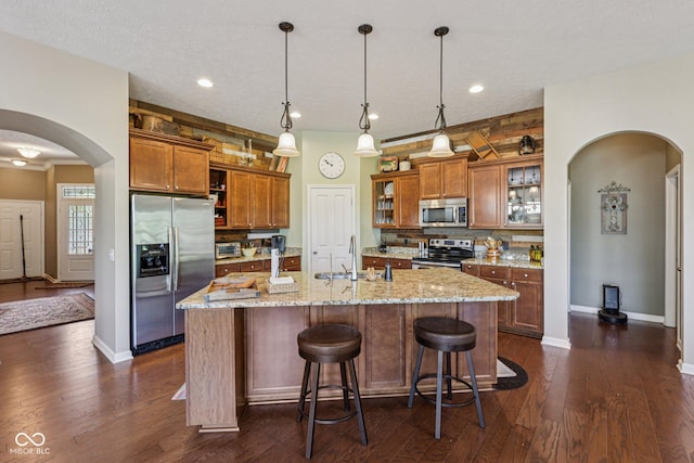 1387 Mayfield Ct, Westfield, IN 46074 - kitchen featuring stainless steel appliances, brown cabinetry, arched walkways, backsplash, and dark wood finished floors
