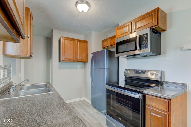 3426 N Olney St, Indianapolis, IN 46218 - kitchen with stainless steel appliances, light wood-style flooring, a textured ceiling, and brown cabinetry