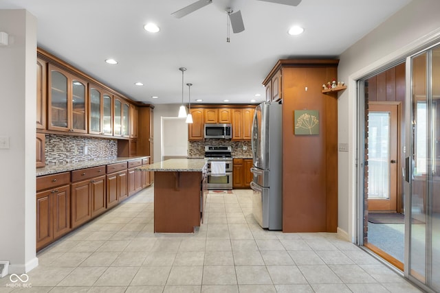 3905 Cove Rd, Columbus, IN 47203 - kitchen with appliances with stainless steel finishes, a ceiling fan, a center island, backsplash, and light stone counters