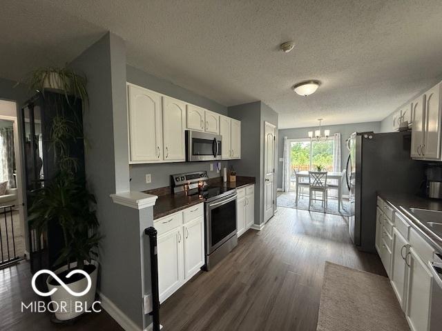 5714 High Timber Ln, Indianapolis, IN 46235 - kitchen featuring appliances with stainless steel finishes, dark wood finished floors, dark countertops, a chandelier, and white cabinets