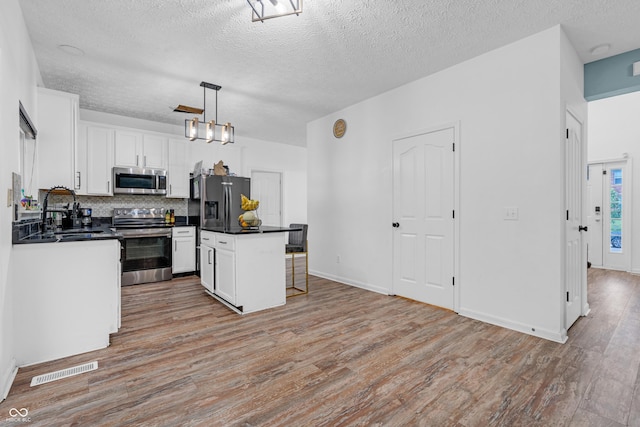 10249 Winlee Ct, Indianapolis, IN 46236 - kitchen featuring appliances with stainless steel finishes, dark countertops, light wood finished floors, white cabinetry, and backsplash