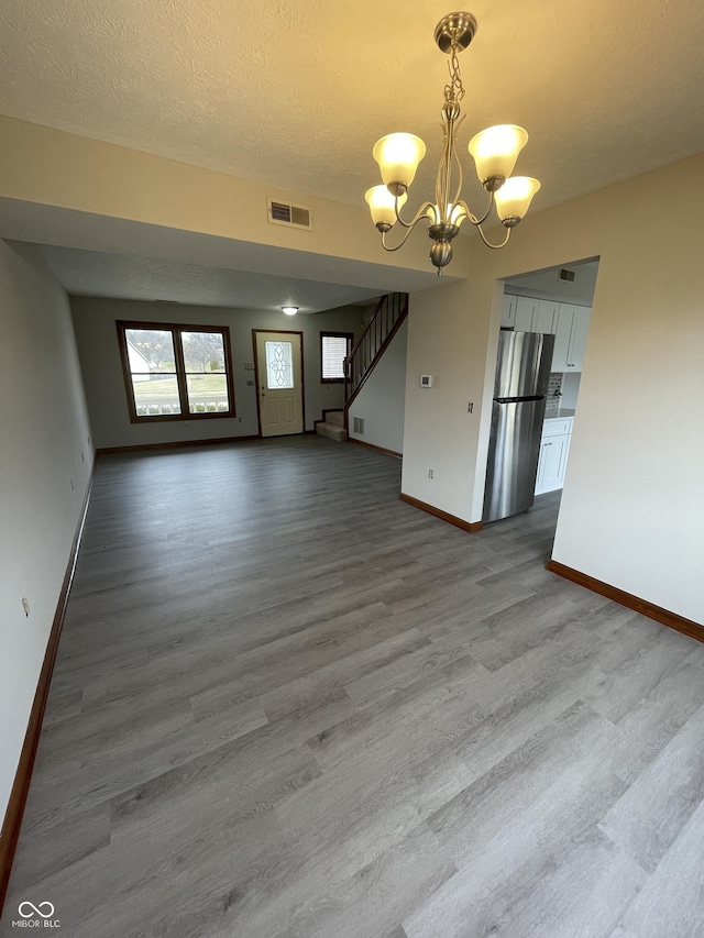 2068 Suda Dr, Carmel, IN 46280 - unfurnished living room with a chandelier, wood finished floors, stairway, and a textured ceiling