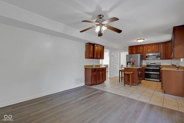 8850 Tanner Dr, Fishers, IN 46038 - kitchen with appliances with stainless steel finishes, a kitchen island, a ceiling fan, light countertops, and a breakfast bar