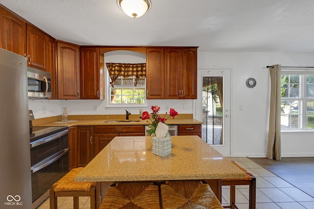 8850 Tanner Dr, Fishers, IN 46038 - kitchen with stainless steel appliances, a breakfast bar area, light tile patterned floors, light stone counters, and a textured ceiling