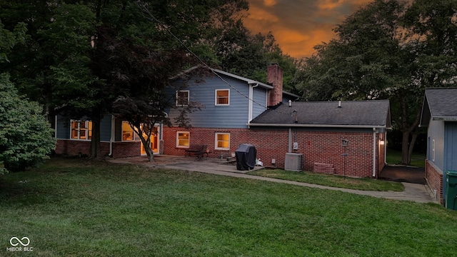 812 Eaglewood Dr, Zionsville, IN 46077 - back of house at dusk with brick siding, a patio, a chimney, and a lawn