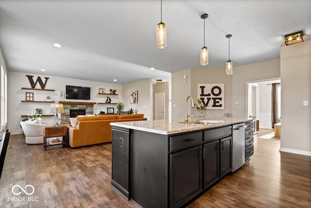 11322 Sea Side Ct, Fishers, IN 46040 - kitchen with stainless steel dishwasher, dark wood-style flooring, a kitchen island with sink, decorative light fixtures, and a stone fireplace