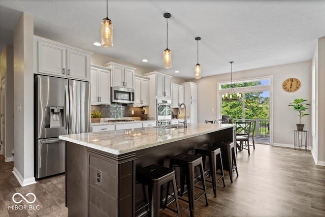 11322 Sea Side Ct, Fishers, IN 46040 - kitchen featuring appliances with stainless steel finishes, dark wood finished floors, a kitchen island with sink, backsplash, and white cabinetry