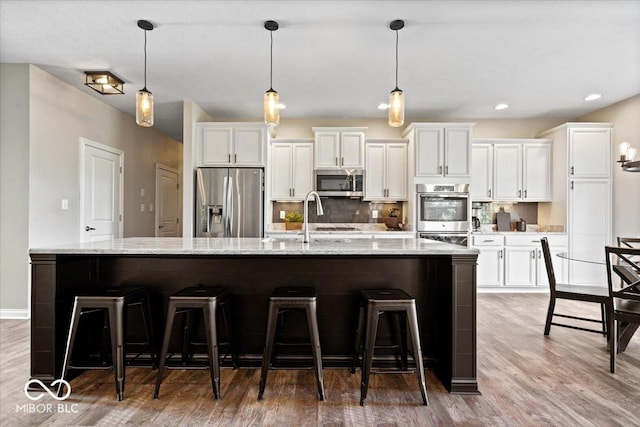 11322 Sea Side Ct, Fishers, IN 46040 - kitchen featuring appliances with stainless steel finishes, white cabinetry, a large island with sink, light wood finished floors, and a kitchen bar