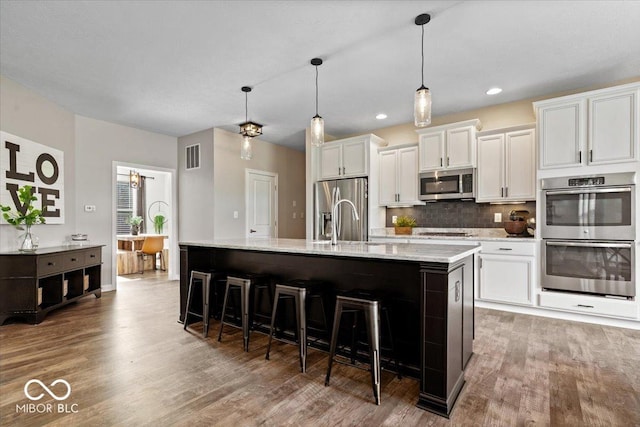 11322 Sea Side Ct, Fishers, IN 46040 - kitchen with stainless steel appliances, wood finished floors, white cabinetry, a kitchen island with sink, and recessed lighting
