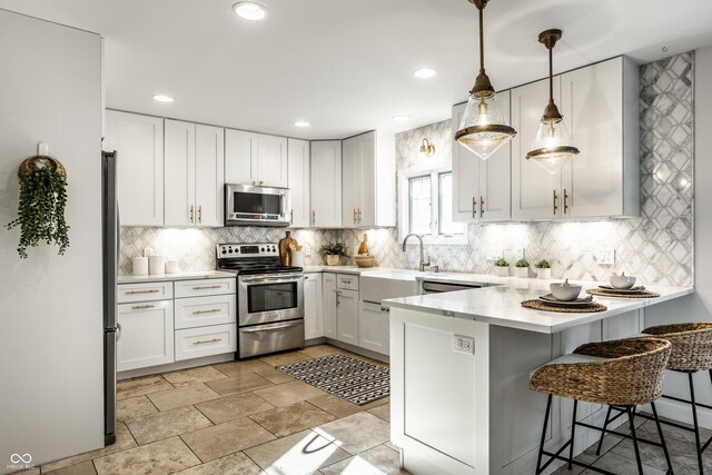 8627 Emerald Ln, Indianapolis, IN 46260 - kitchen with appliances with stainless steel finishes, a peninsula, light countertops, decorative backsplash, and a breakfast bar