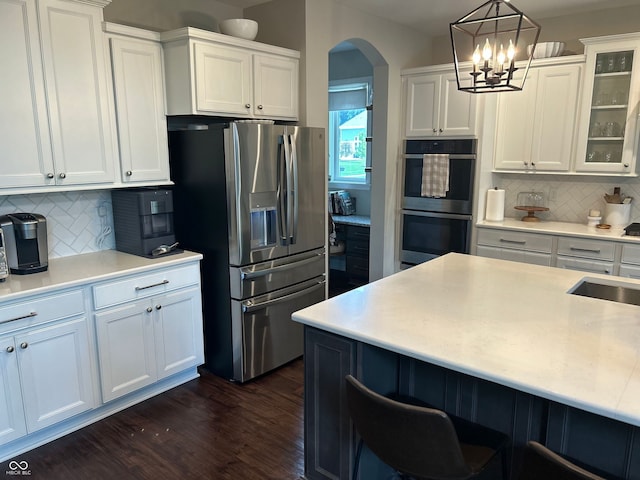 12059 Chapelwood Dr, Fishers, IN 46037 - kitchen featuring appliances with stainless steel finishes, arched walkways, decorative backsplash, glass insert cabinets, and white cabinetry