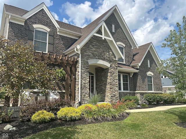 12059 Chapelwood Dr, Fishers, IN 46037 - view of front of property featuring stone siding, roof with shingles, a front yard, brick siding, and a pergola