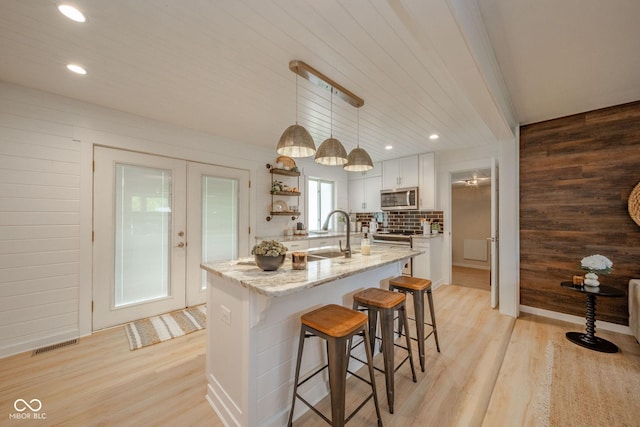 107 Pasadena Rd, Noblesville, IN 46062 - kitchen with stainless steel microwave, light wood-style floors, wood walls, a center island with sink, and white cabinetry
