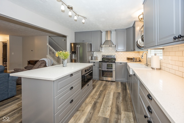 14126 Stonewood Pl, Fishers, IN 46037 - kitchen with gray cabinetry, appliances with stainless steel finishes, wall chimney exhaust hood, and dark wood finished floors