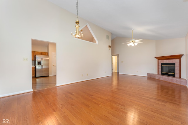 11628 Coastal Way, Indianapolis, IN 46229 - unfurnished living room with high vaulted ceiling, a tiled fireplace, a ceiling fan, light wood-style floors, and a chandelier