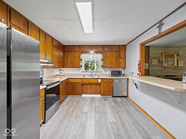 5530 Skyridge Dr, Indianapolis, IN 46250 - kitchen featuring stainless steel appliances, a textured ceiling, light wood-type flooring, under cabinet range hood, and brown cabinets