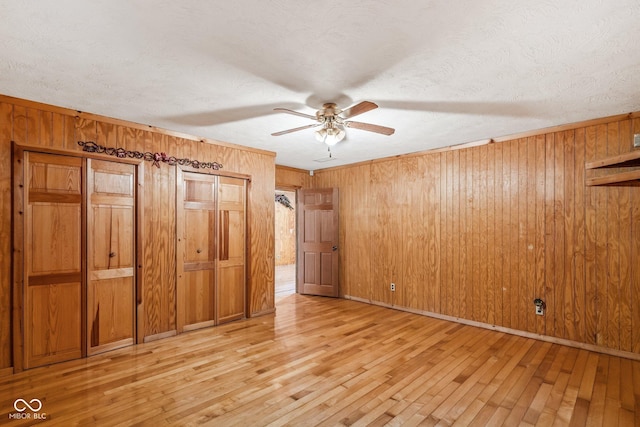 8701 E Splinter Ridge Rd, Madison, IN 47250 - unfurnished bedroom featuring wooden walls, light wood-style floors, a textured ceiling, two closets, and ceiling fan