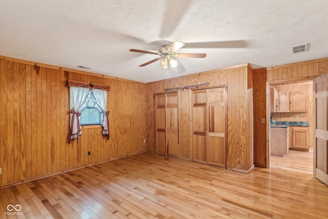 8701 E Splinter Ridge Rd, Madison, IN 47250 - unfurnished bedroom with light wood finished floors, wood walls, ceiling fan, and a textured ceiling