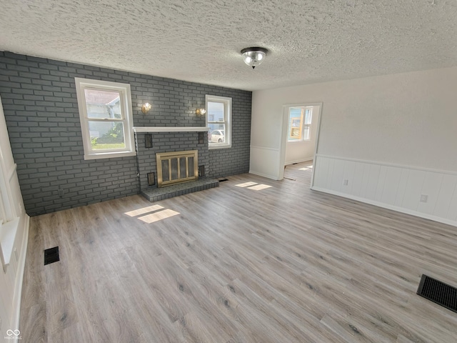 316 E Mechanic St, Shelbyville, IN 46176 - unfurnished living room with a textured ceiling, brick wall, a brick fireplace, wood finished floors, and wainscoting