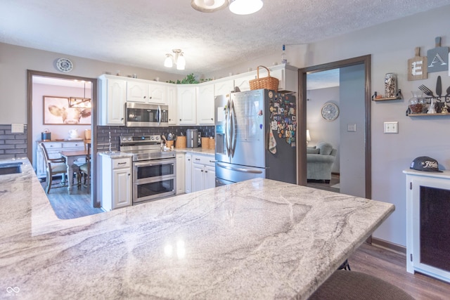 5237 Honey Comb Ln, Indianapolis, IN 46221 - kitchen featuring appliances with stainless steel finishes, wood finished floors, white cabinets, a peninsula, and tasteful backsplash