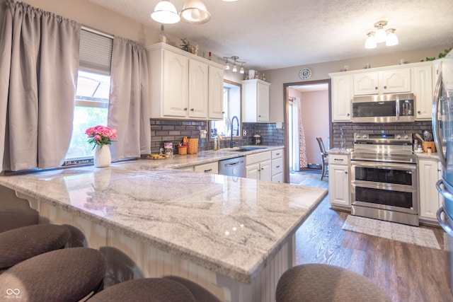 5237 Honey Comb Ln, Indianapolis, IN 46221 - kitchen with appliances with stainless steel finishes, a peninsula, decorative backsplash, white cabinetry, and a textured ceiling
