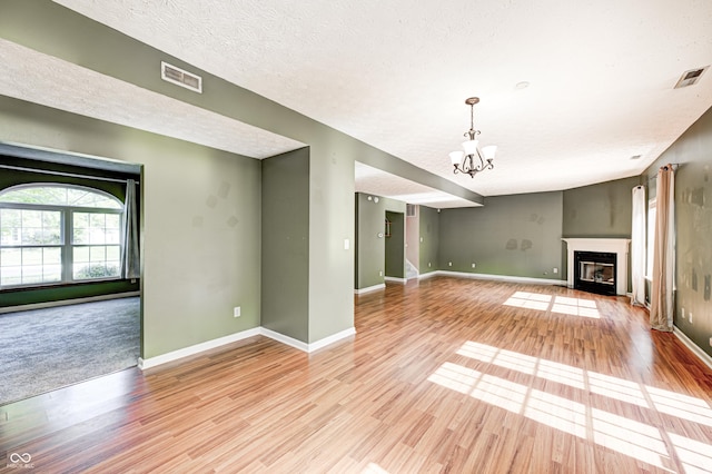 1143 Kinross Dr, Avon, IN 46123 - unfurnished living room featuring a chandelier, light wood finished floors, a fireplace with flush hearth, and a textured ceiling