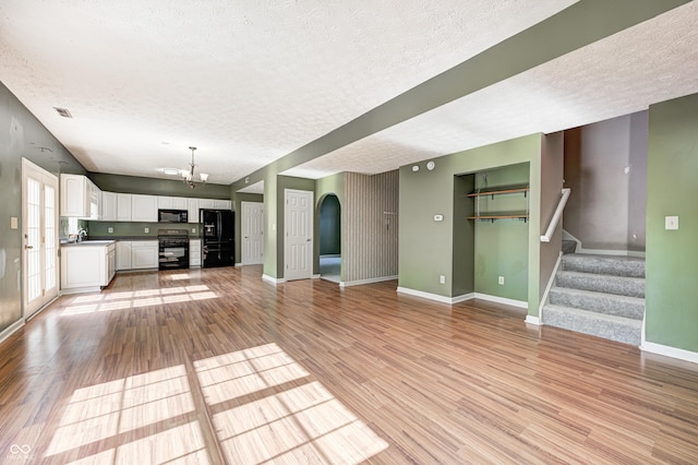 1143 Kinross Dr, Avon, IN 46123 - unfurnished living room featuring a textured ceiling, a chandelier, light wood-style floors, stairs, and arched walkways
