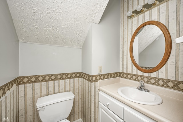 1143 Kinross Dr, Avon, IN 46123 - half bath featuring a textured ceiling, vaulted ceiling, vanity, wainscoting, and wallpapered walls