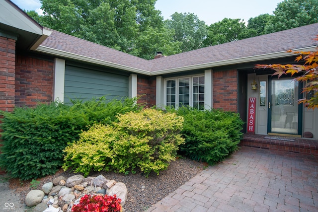 8841 Rocky Ridge Rd, Indianapolis, IN 46217 - view of exterior entry with brick siding, a shingled roof, a chimney, and an attached garage