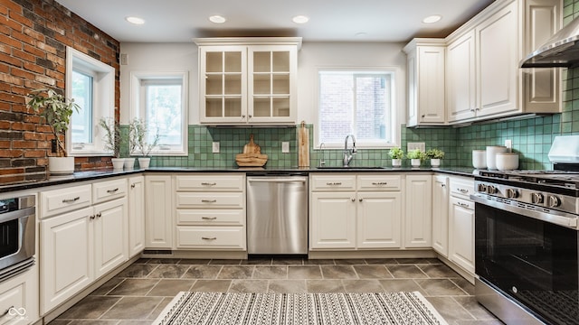 5809 N Washington Blvd, Indianapolis, IN 46220 - kitchen featuring appliances with stainless steel finishes, wall chimney exhaust hood, dark countertops, glass insert cabinets, and backsplash