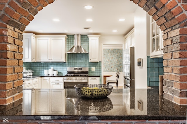5809 N Washington Blvd, Indianapolis, IN 46220 - kitchen featuring wall chimney range hood, appliances with stainless steel finishes, arched walkways, tasteful backsplash, and a peninsula