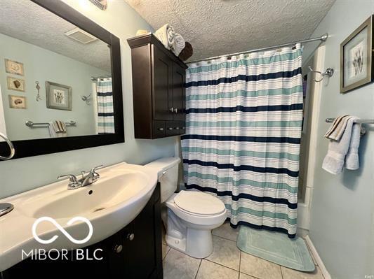 9406 S Lake Ridge Dr, Bloomington, IN 47401 - full bathroom with a textured ceiling, vanity, tile patterned flooring, and shower / bath combo with shower curtain