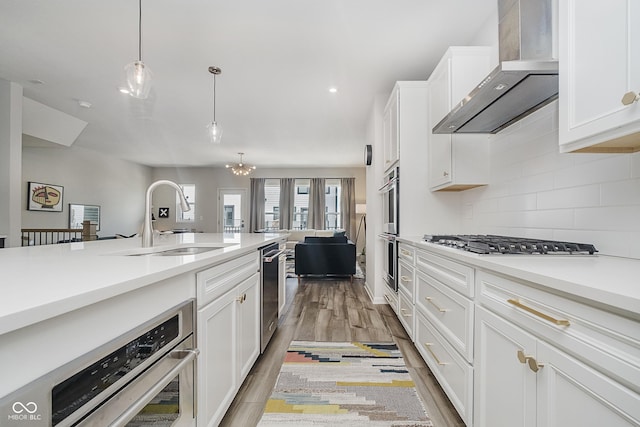 9732 Junction, Fishers, IN 46037 - kitchen with wall chimney exhaust hood, light wood-style floors, backsplash, white cabinetry, and hanging light fixtures