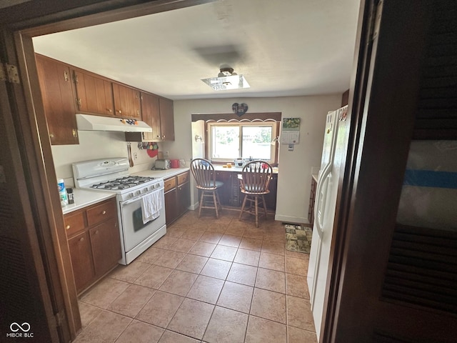 9012 W Evergreen Dr, Columbus, IN 47201 - kitchen with white appliances, under cabinet range hood, light countertops, light tile patterned flooring, and brown cabinets