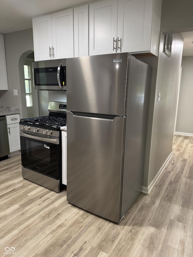 67 N Devon Ave, Indianapolis, IN 46219 - kitchen featuring stainless steel appliances, arched walkways, light wood-style floors, and white cabinetry