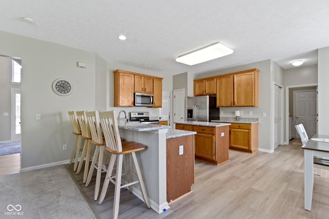 441 Viburnum Run, Westfield, IN 46074 - kitchen with a peninsula, appliances with stainless steel finishes, light wood-style flooring, light stone countertops, and a breakfast bar