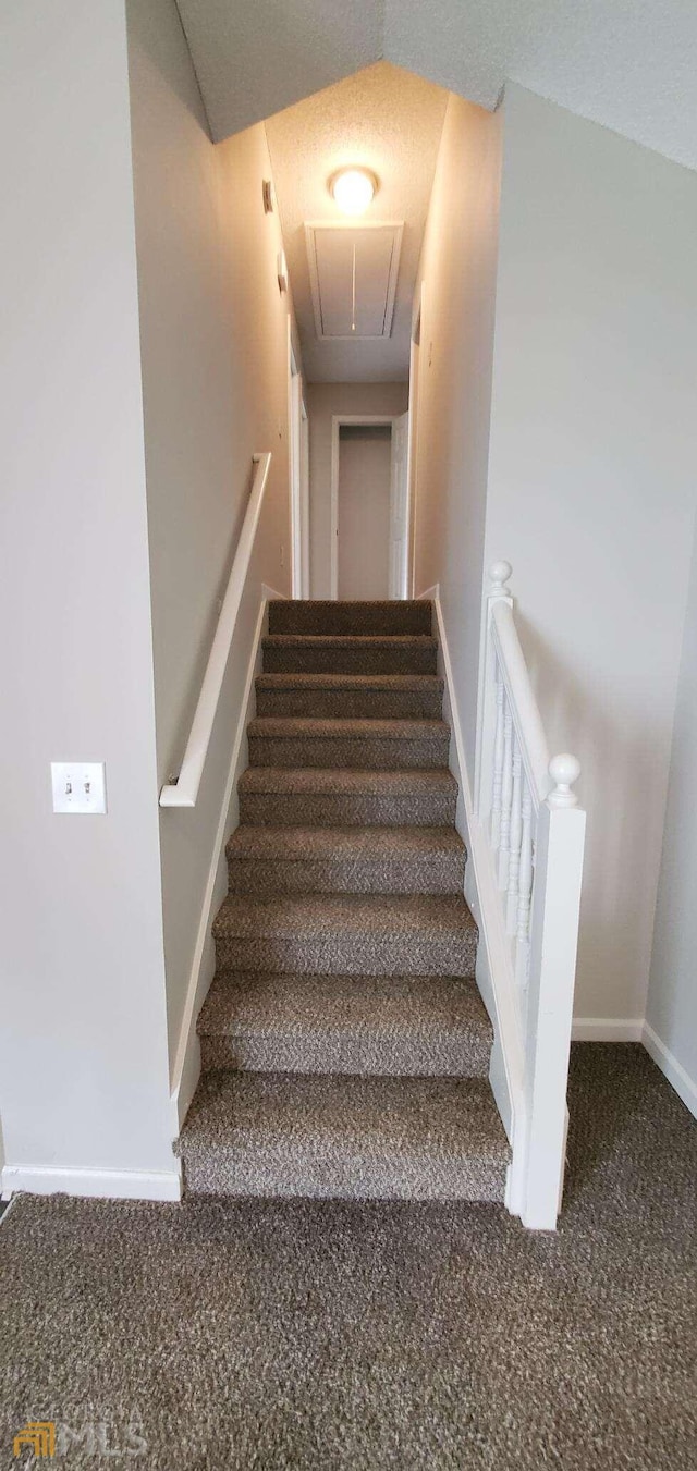 stairway featuring lofted ceiling and dark colored carpet