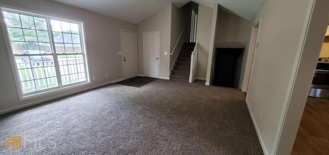 spare room featuring plenty of natural light, vaulted ceiling, and dark colored carpet