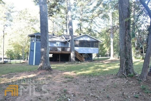 back of house featuring a wooden deck, a sunroom, and a lawn