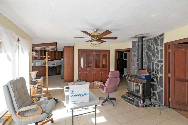 home office featuring light tile floors, a textured ceiling, ceiling fan, and a wood stove