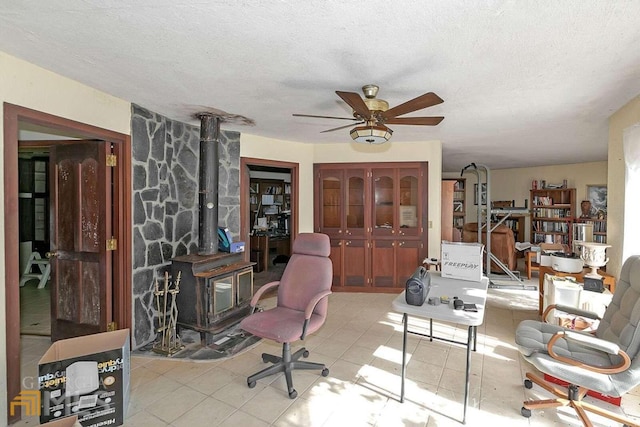 office space with light tile floors, ceiling fan, a wood stove, and a textured ceiling